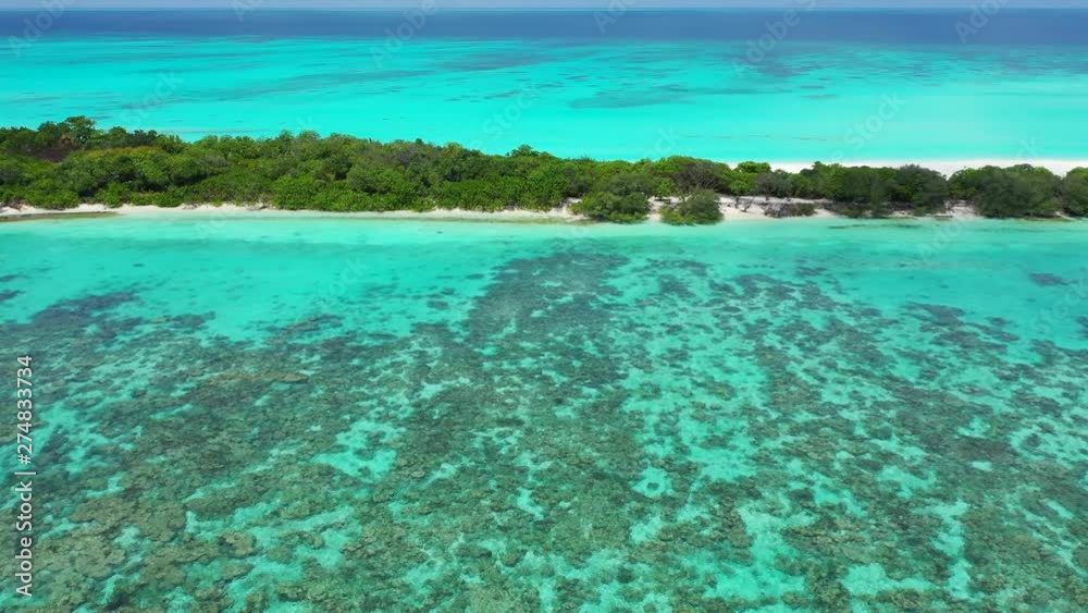 Aerial view of a tropical island with trees on it. Turquoise blue water with some reefs in it, in the foreground. In Jamaica  Dolly out