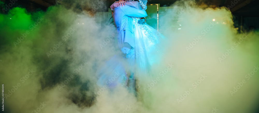First wedding dance of a couple. Beautiful lights and luxury dress. Bride and groom in love hugging. First wedding dance of a couple. Beautiful lights and luxury dress. Bride and groom in love hugging.