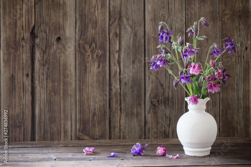 Fototapet aquilegia flowers in white vase on old wooden background