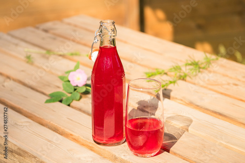 glass bottle with a red cold drink on a wooden table in the sunshine