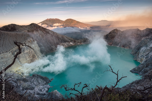 Active volcano crater with turquoise lake and sulfur smoke in the morning