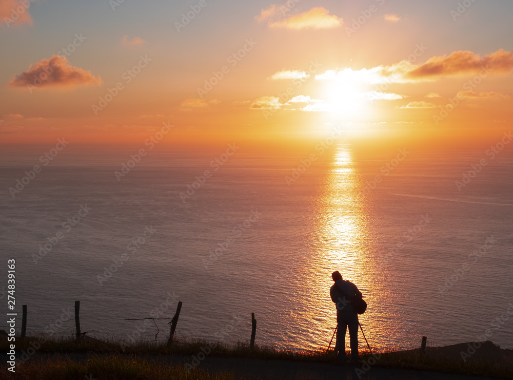Man photographing the sun over the sea at sunset, Basque Country