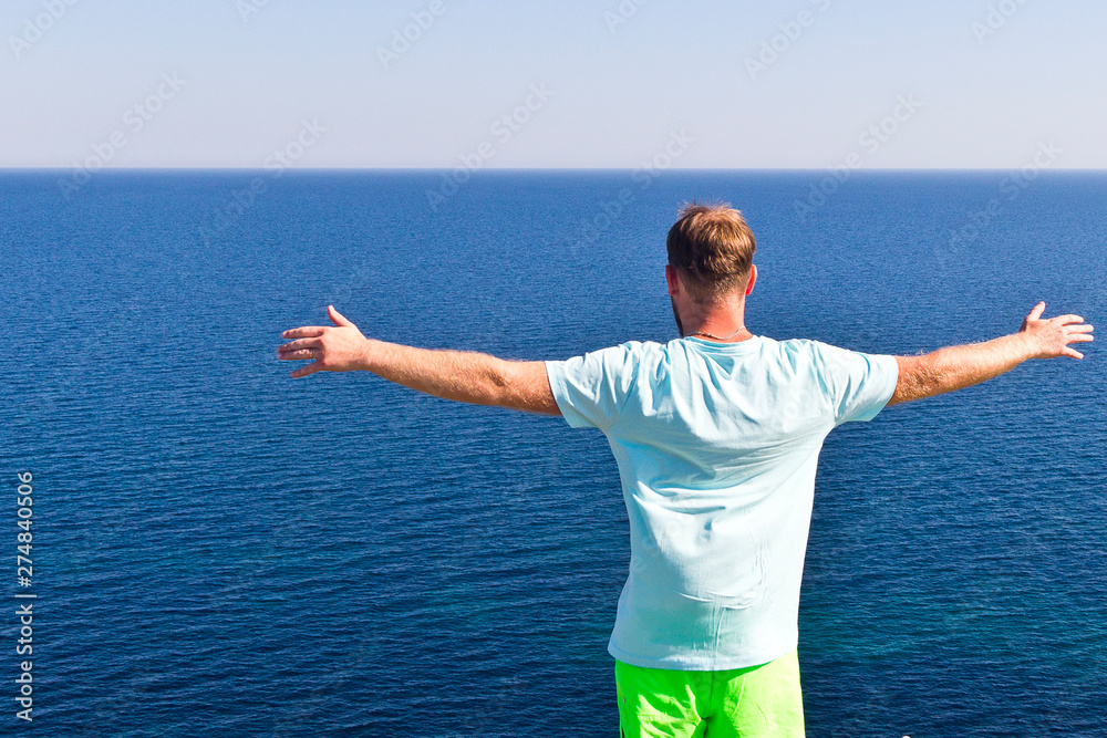 a young man with his arms outstretched is standing on the edge of a precipice and admiring the gorgeous views of the sea a young man with his arms outstretched is standing on the edge of a precipice and admiring the gorgeous views of the sea