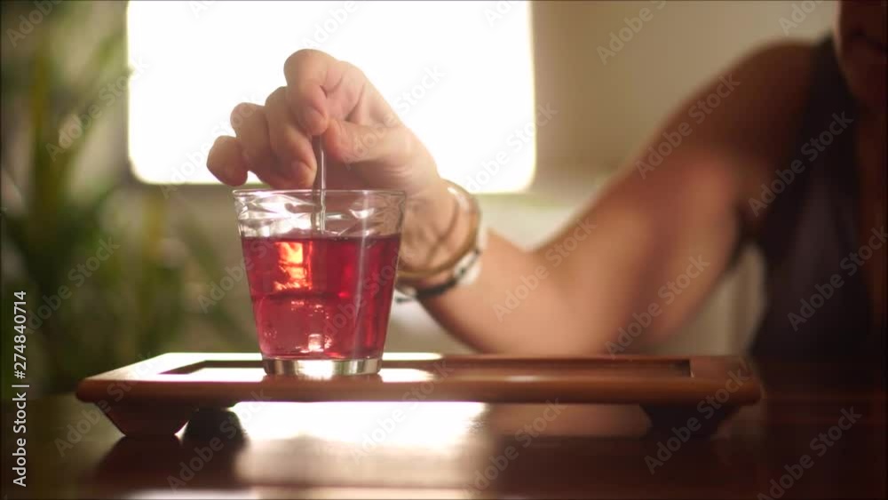 Middle aged brunette woman mixing her pink cocktail with a glass stick.