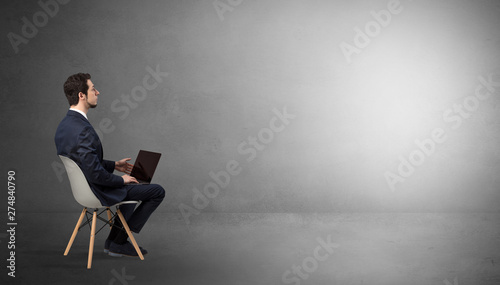 Businessman staying in an empty grey dark room with stuffs on his lap 