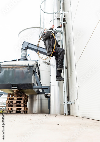 Chimney sweep cleaning a chimney standing balanced on the apex of a house roof lowering equipment down the flue