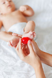 Mother holds newborn baby's feet. Tiny fingers and red massage ball in woman's hand. Cozy morning at home.