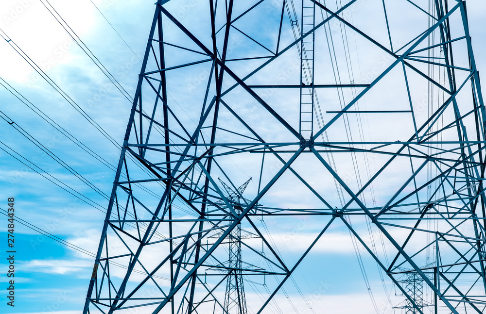 High voltage electric tower and transmission lines. Electricity pylons with blue sky and white clouds. Power and energy conservation. High voltage grid tower with wire cable at distribution station.