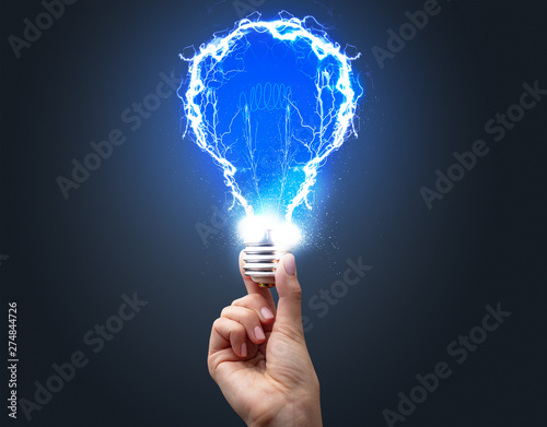 Hand holding shiny light bulb on dark background. New idea concept