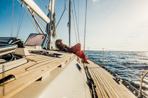 Warm filter relax concept for happy people on summer vacation - nice curly woman lay down on a sail boat enjoying the trip and taking a sunbath - wanderlust and tourist concept