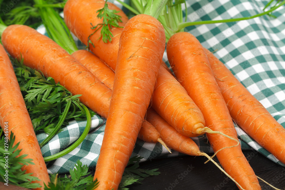 Fresh carrots on checkered tablecloth close up