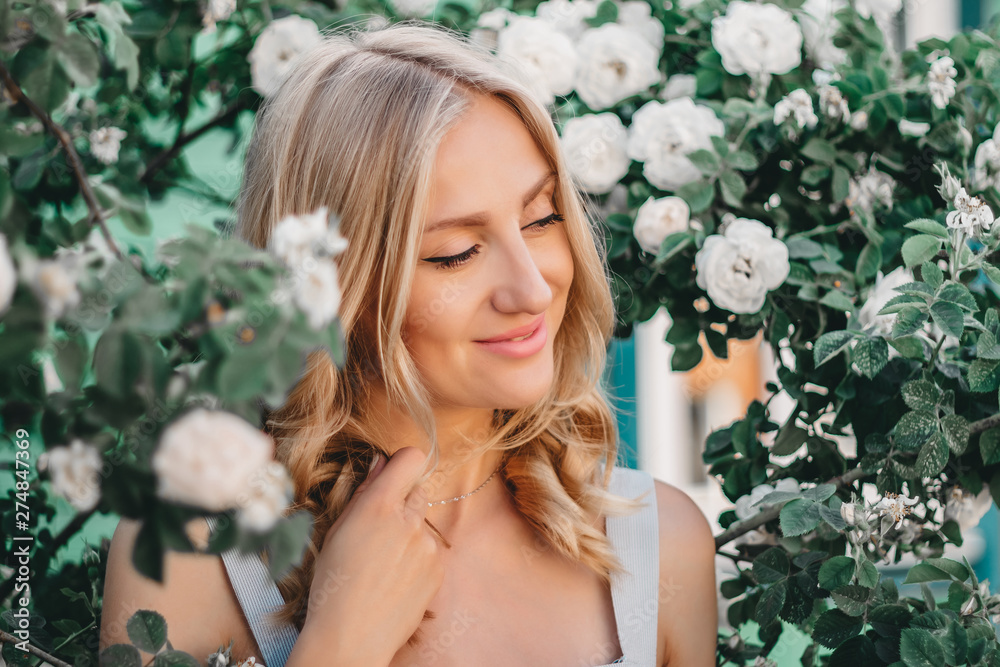 Portrait of a beautiful blonde girl with hairstyle on the background of a bush of white roses. Wedding photosession Portrait of a beautiful blonde girl with hairstyle on the background of a bush of white roses. Wedding photosession