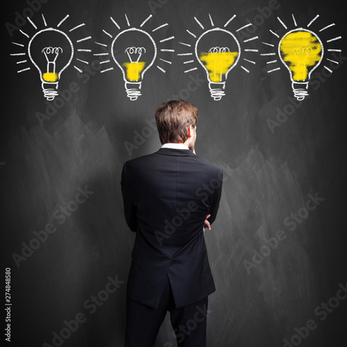 successful businessman standing in front of a blackboard with lightbulbs, symbolizing having an idea in development