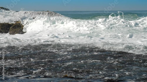 foaming ocean waves roll on brown rock near coastline on sunny summer day slow motion. Concept tsunami impact and ecosystem change photo