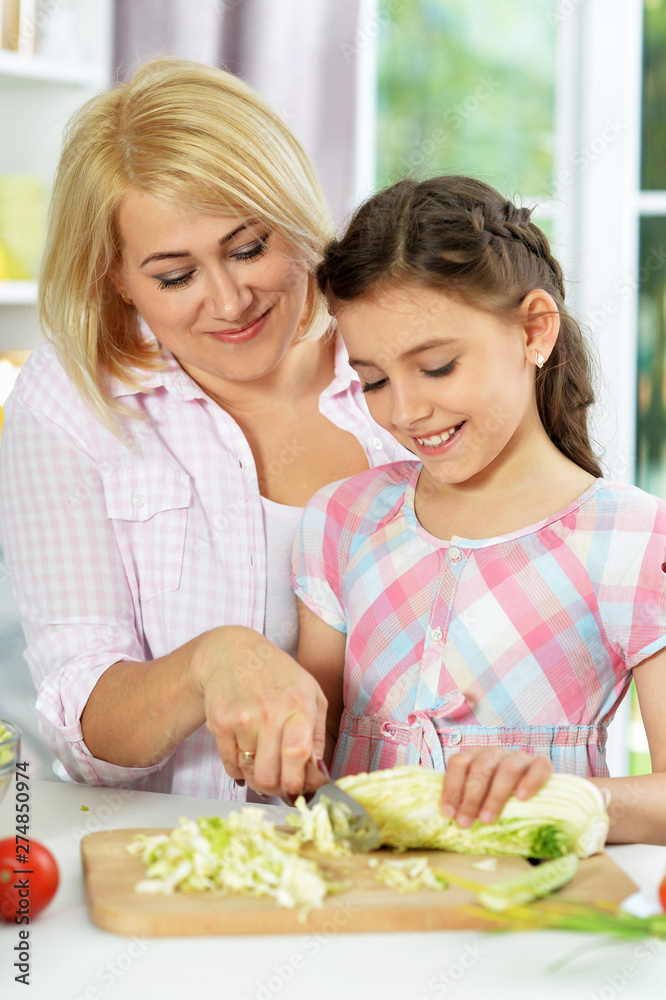 Cute little girl with her mother cooking together at kitchen table