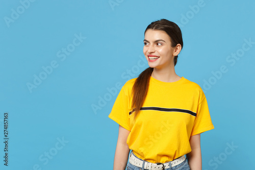 Portrait of cheerful smiling beautiful young woman in vivid casual clothes standing and looking aside isolated on bright blue wall background in studio. People lifestyle concept. Mock up copy space.