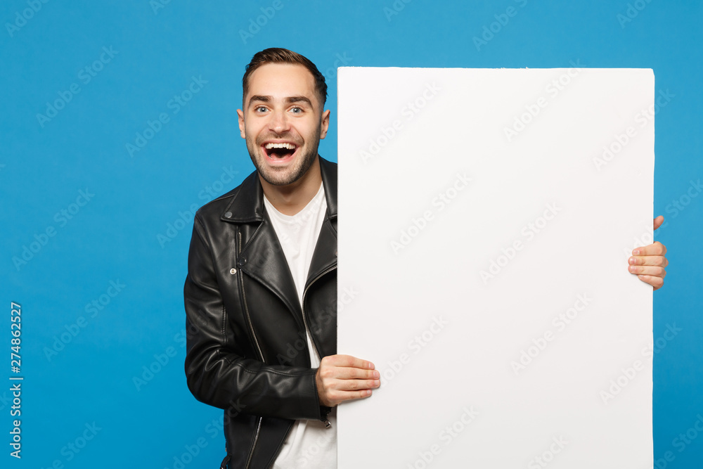 Handsome young bearded man hold big white empty blank billboard for promotional content isolated on blue wall background studio portrait. People sincere emotions lifestyle concept. Mock up copy space. Handsome young bearded man hold big white empty blank billboard for promotional content isolated on blue wall background studio portrait. People sincere emotions lifestyle concept. Mock up copy space.