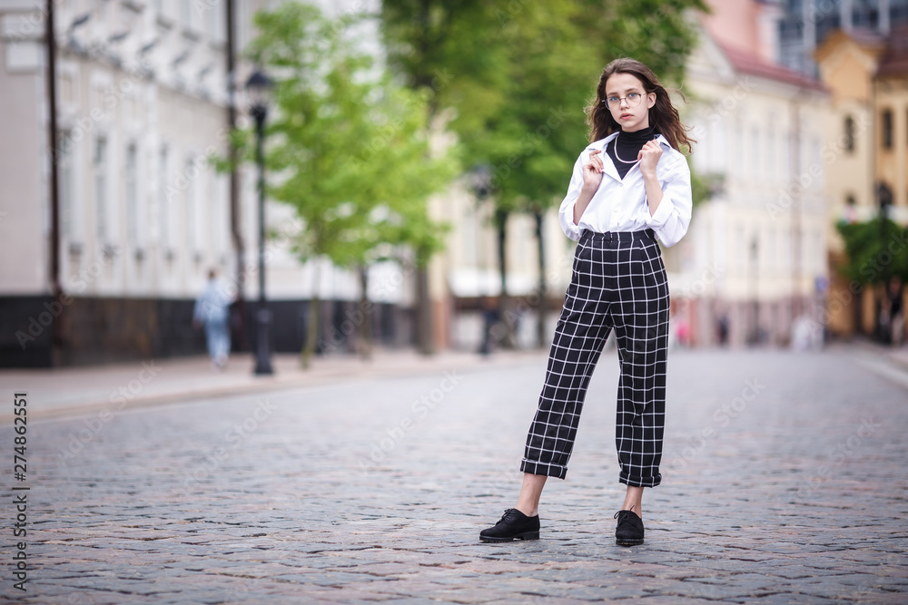 portrait of little beautiful stylish kid girl with sunglasses and short plaid pants in city urban street