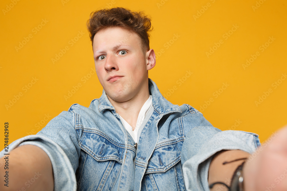 Close up selfie shot of shocked young man in denim casual clothes looking camera isolated on yellow orange wall background in studio. People sincere emotions lifestyle concept. Mock up copy space. Close up selfie shot of shocked young man in denim casual clothes looking camera isolated on yellow orange wall background in studio. People sincere emotions lifestyle concept. Mock up copy space.