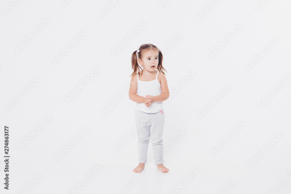 a little girl indulges in a white background: dancing, shy, shows her thumb