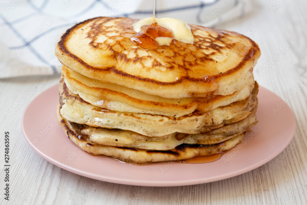 Homemade pancakes with butter and maple syrup on a pink plate, side view. Closeup. Homemade pancakes with butter and maple syrup on a pink plate, side view. Closeup.