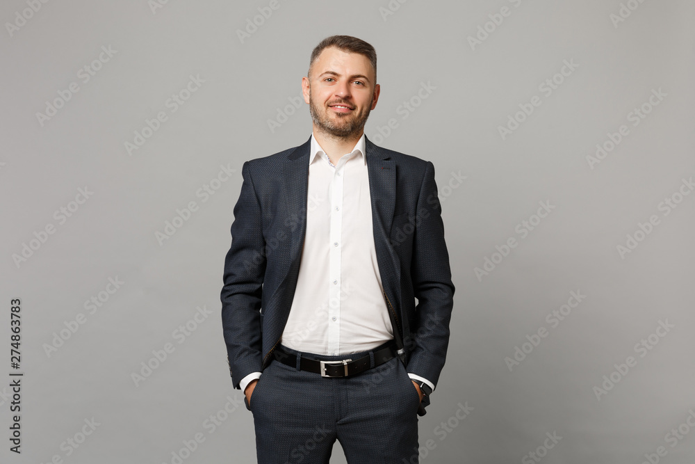 Fototapeta premium Handsome successful confident young business man in classic black suit shirt posing isolated on grey wall background, studio portrait. Achievement career wealth business concept. Mock up copy space.