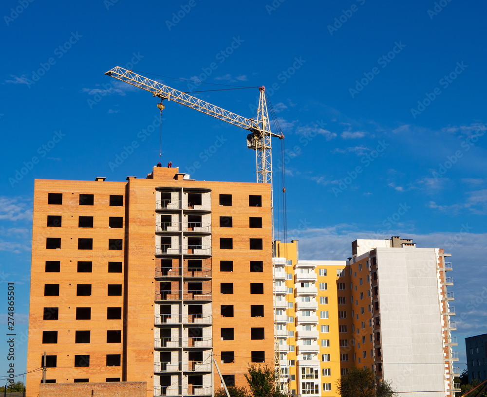 Unfinished brick multistory building with crane on the construction site, condo