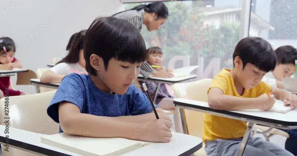 Little boy writing to book at classroom. Teacher take care to her student for lesson. Education concept. Little boy writing to book at classroom. Teacher take care to her student for lesson. Education concept.