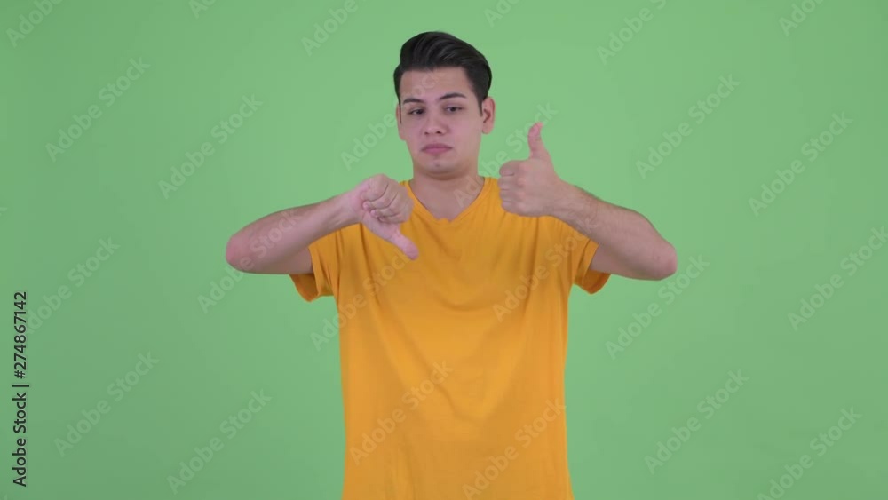 Happy young multi ethnic man giving choosing between thumbs up and thumbs down Happy young multi ethnic man giving choosing between thumbs up and thumbs down