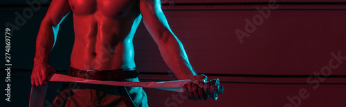 panoramic shot of sexy fireman holding fire hose in darkness photo