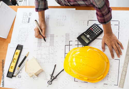 Construction and building concept. Engineers or architect holding a pen with drawings in construction on blueprints in office.