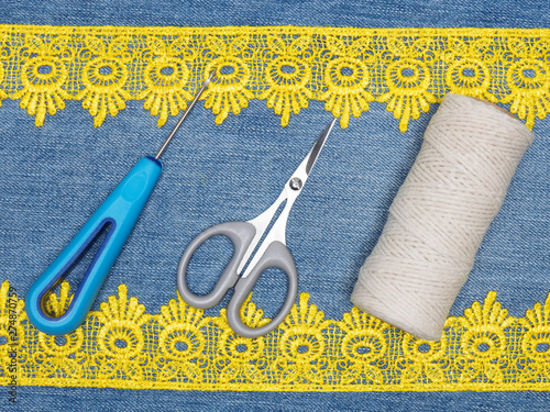 Yellow lace, awl, scissors and thread on a jeans background. Sewing still life photo