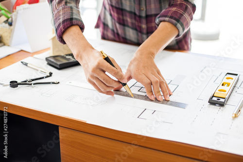 Construction and building concept. Engineers or architect holding a pen with drawings in construction on blueprints in office.