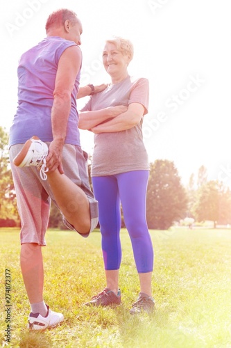 Senior man performing quad stretch while taking support of woman in park