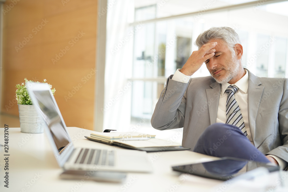Exhausted businessman sitting at desk in office Exhausted businessman sitting at desk in office