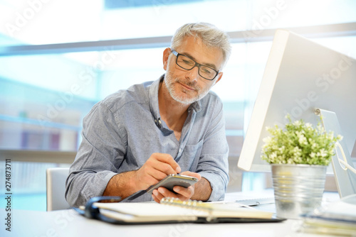 Casual mature businessman working on cellphone in modern office