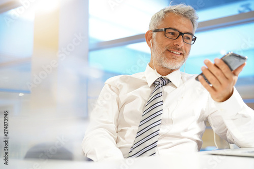Businessman talking on cellphone with headphones in contemporary office