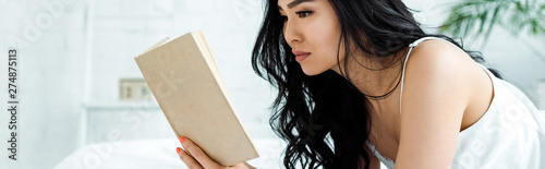 panoramic shot of brunette thai woman reading book at home