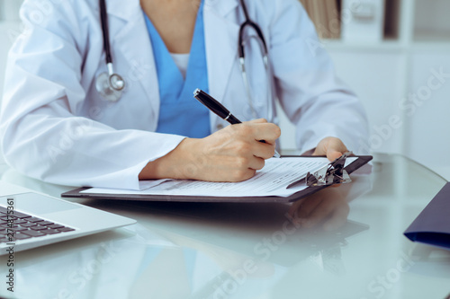 Doctor woman filling up medical form while sitting at the table  close-up of hands