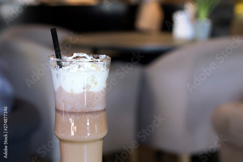 Hot coffee drink with whipped cream in glass, black straw in cafe. Close-up, copy space, toned