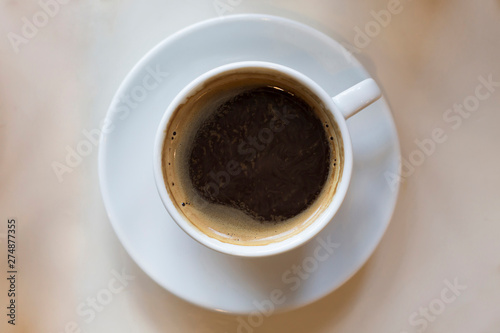 Cup of black coffee on white plate on beige table. Top view, flat lay, copy space, mock up © Anna
