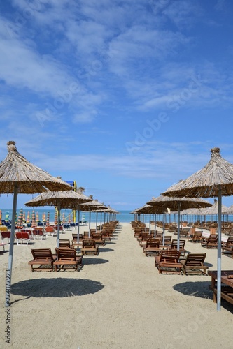 Umbrellas and chaise lounges on the sandy beach. Wooden beach chairs  beds and straw umbrella on a tropical beach. Deck chairs and umbrellas on a sandy beach. Summer holiday season concept