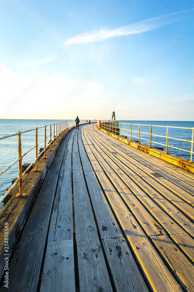 Fototapeta premium WHITBY, ENGLAND Tourists visiting Whitby Pier and lighthouse. 12/05/2019