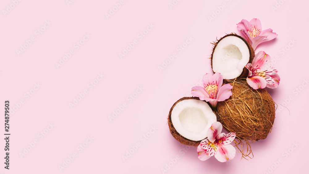 Broken coconut with tropic flowers on pink background.