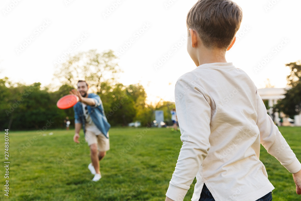 Young man having fun with his little brother or son outoors in park beautiful green grass play game.