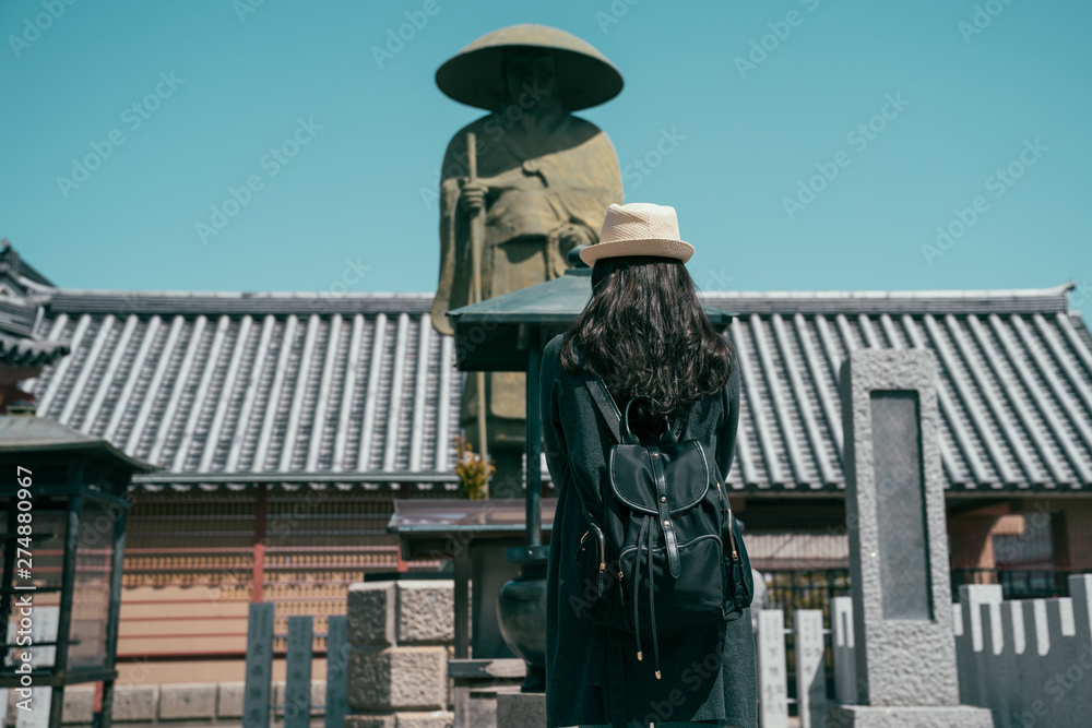 vintage style back view of girl backpacker pray in peaceful shrine under blue sky. woman traveler gracing to statue in the grounds of shitennoji temple in osaka japan. female tourist on summer trip