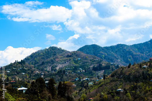 Mountain village. Village in mountains, green forest, blue sky and white clouds.