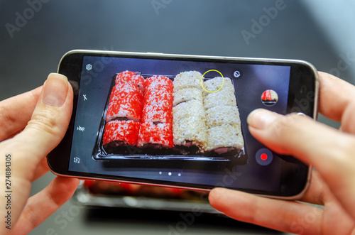 A girl photographs red and white sushi on the phone from different angles. Photo close up.