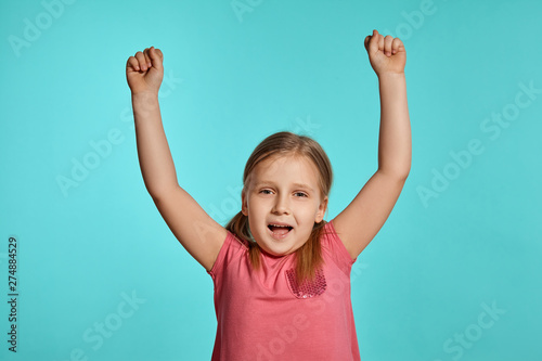 Close-up shot of beautiful blonde little girl in a pink dress posing against a blue background.