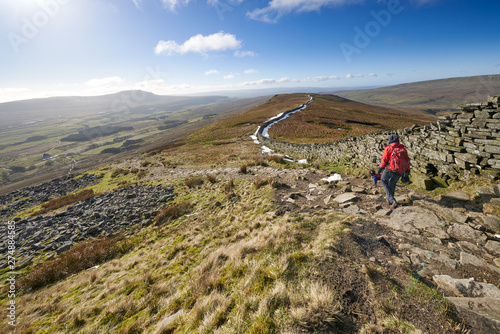 A hiker walking down from the summit of Whernside, part of the Three Peaks with Sand Beds Head Pike in the distance. The Yorkshire Dales, England. photo